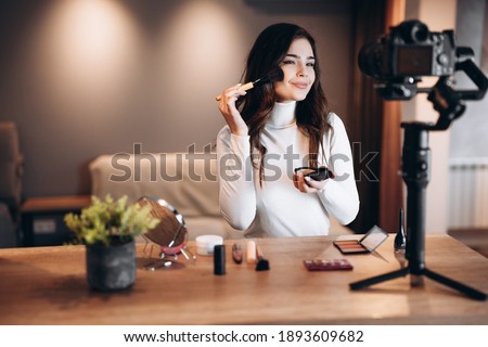 Beauty blogger pretty female filming daily make-up routine tutorial on camera. Influencer young woman live streaming cosmetics product review in home studio. Vlogger job. DIY putting makeup Royalty-Free Stock Photo #1893609682