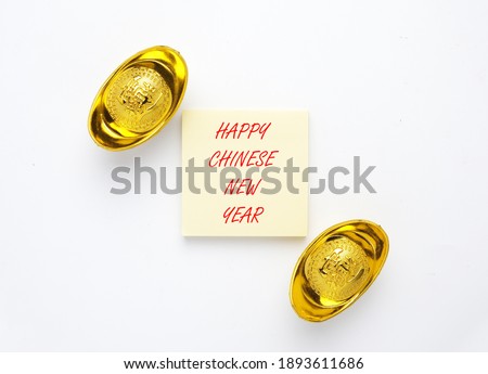 A picture of Happy Chinese New Year on notepad and golden ingot or "yuan bao" written in chinese for prosperity on isolated white background. 