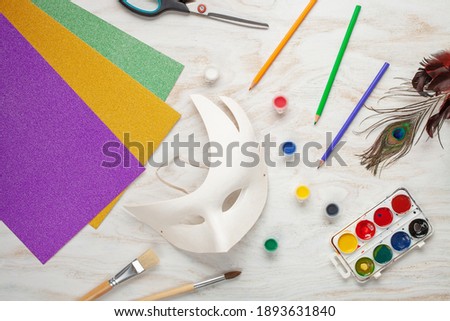 Paper Carnival mask and paints DIY on a white wooden background. Mardi Gras concept. Top view