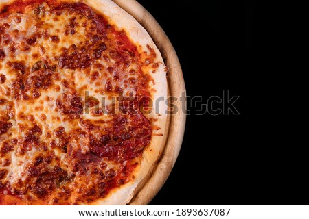 Tasty pizza made with pepperoni and ham, served on a wood board. Mozzarella topping melted on top. Isolated on black background. Free space for text. Professional close up photography.