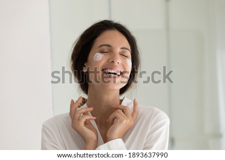 Close up of happy young Caucasian woman do daily morning beauty procedures or treatment in home bath. Smiling lady apply nourishing moisturizing face cream for healthy glowing skin. Skincare concept. Royalty-Free Stock Photo #1893637990