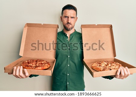Handsome man with beard holding two italian pizzas skeptic and nervous, frowning upset because of problem. negative person. 