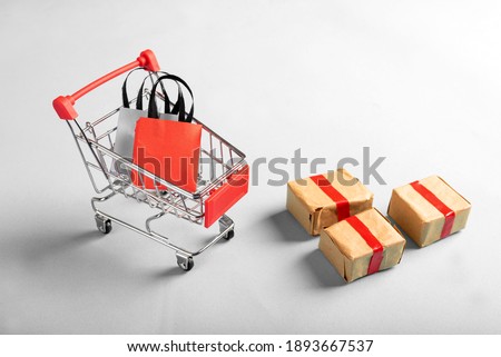 A miniature shopping cart filled with shopping bags while gift boxes are placed outside