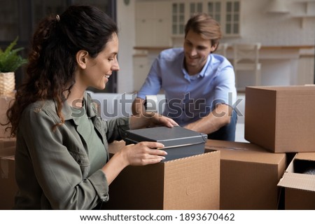 Happy young Caucasian man and woman pack boxes relocate to new house together. Smiling millennial couple renters feel excited moving to own home, do unpacking unboxing. Rental concept. Royalty-Free Stock Photo #1893670462