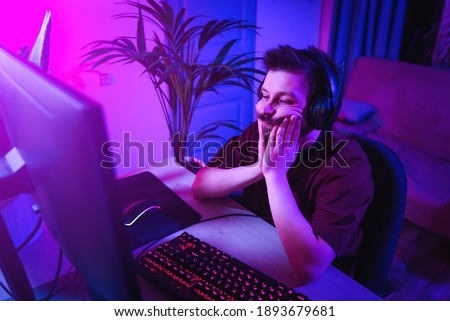 The man plays computer games at home. Young guy is bored during online learning. Neon light in the evening. Weekend at home at the screen.The boy lost, was tired and upset.