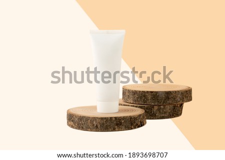 Blank cosmetics tube stand on the top of wooden cut.Two slices behind like podium for product.Beautiful pastel beige isometric background.Organic copcept.