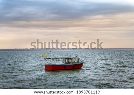 Photo of motor fishing boat under dark clouds with yellow flag