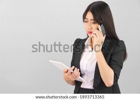 Young Asian women in suit standing using her digital tablet and phone against gray background