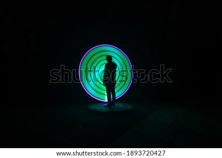 one person standing against beautiful green and purple circle light painting as the backdrop