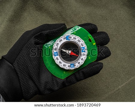 Hand in a black glove holds a compass