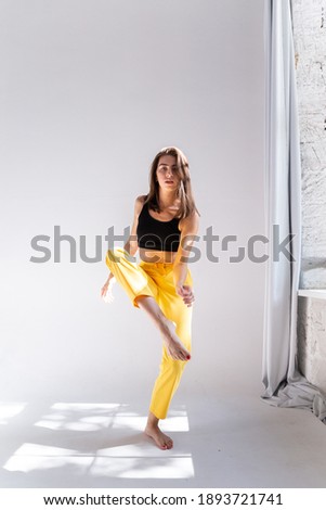 A slender girl in yellow trousers and a sports top is dancing on a white isolated background. Girl athlete on a white isolated background with place for text or logo, doing gymnastic exercises.