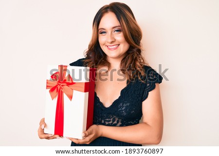 Young beautiful caucasian woman holding gift looking positive and happy standing and smiling with a confident smile showing teeth 