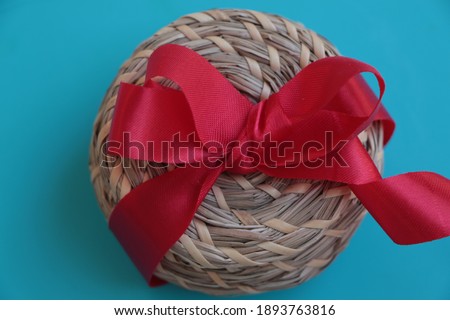 Small wicker gift box tied with a red satin ribbon. Authentic gift box in turquoise blue background. Giving gifts to lover, mother, father, friend etc. Give a gift concept. 