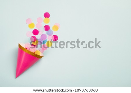 Carnival cap with colorful paper confetti on light blue background. Birthday party, carnival or anniversary card. Top view, flat lay, copy space