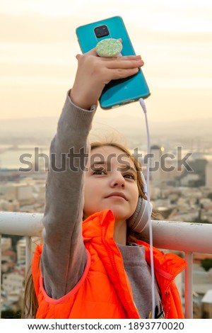 teenage girl with headphones and a bright orange vest taking pictures of herself (selfie) or looking at her smartphone