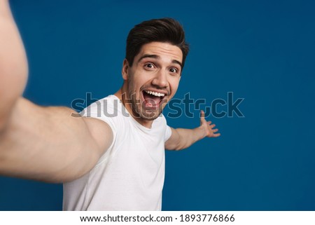 Excited handsome guy showing copyspace while taking selfie isolated over blue background