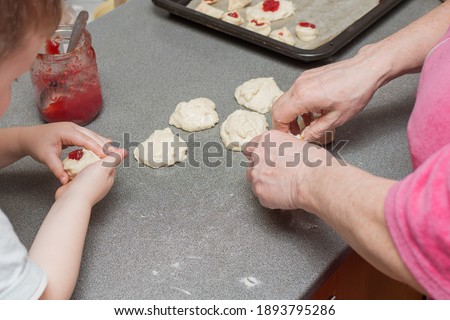 Close-up, top view of the hands of an elderly woman and a child making jam pies. Horizontal photo. The concept is a joint pastime of different generations