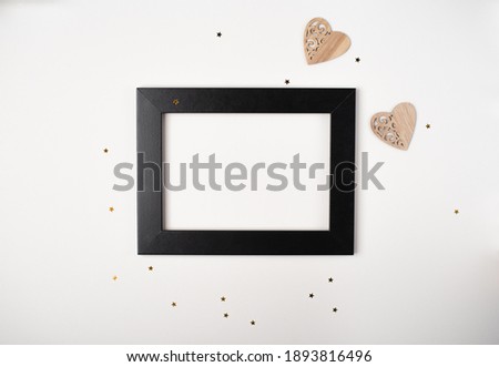 Black photo frame with wooden heart on the white background. Valentine's Day concept. Flat lay, top view, space for text.