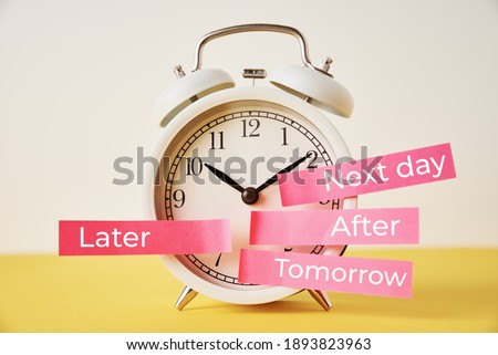 Procrastination, delay and postpone concept. Alarm clock with sticky notes   later, tomorrow, next day and after on the yellow background Royalty-Free Stock Photo #1893823963