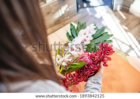 Female florist making flower bouquet. Florist making bouquets at a table in her flower shop. Joyful florist holding flowers for bouquet in hand while preparing it for a client