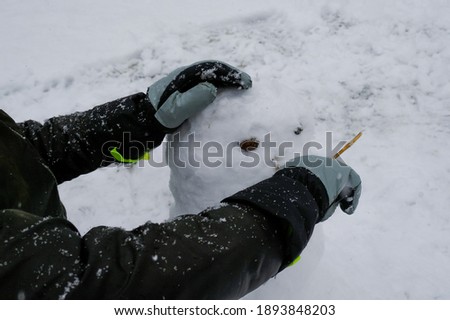 person's hands in gloves making snowman close-up across snowy surface. Winter outdoors activity