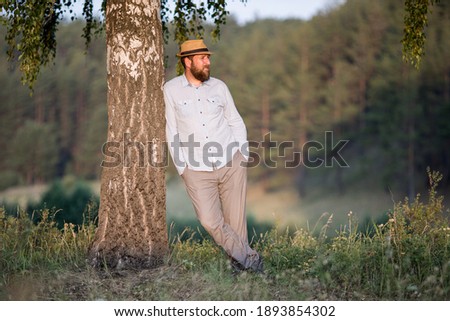a sad man leaning his shoulder against a tree and looking to the future. back ofn green forest in summer