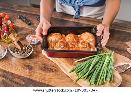A girl prepares to bake a drumstick in the oven.Chicken drumstick in a baking tray stands on the table.