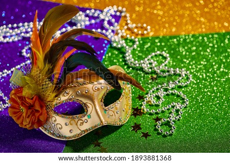 Festive, colorful Mardi Gras or carnivale mask and beads on golden, green and purple background. Venetian masks. Party invitation, greeting card, venetian carnivale celebration concept.