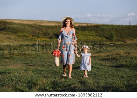 Young mother walking with her little daughter in the green field. Family holiday in garden. Portrait mom with child together on nature. Mum, little daughter outdoors. Happy Mothers Day. Close up