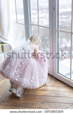 a little girl stands at the window leaning against an ottoman