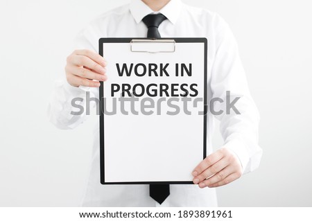 man holding a chalkboard in front of his face with the text work in progress written in it on a gray background