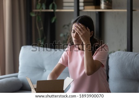 Unhappy millennial indian Arabic woman displeased with wrong order unpacking box shopping online. Upset young ethnic female client or customer dissatisfied with bad quality product unboxing at home. Royalty-Free Stock Photo #1893900070