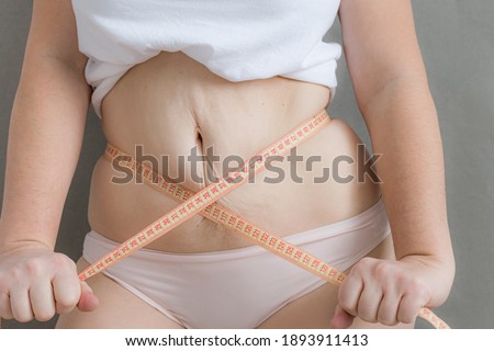 fat woman measuring waist holding centimeter on belly isolated gray background theme of frills Royalty-Free Stock Photo #1893911413