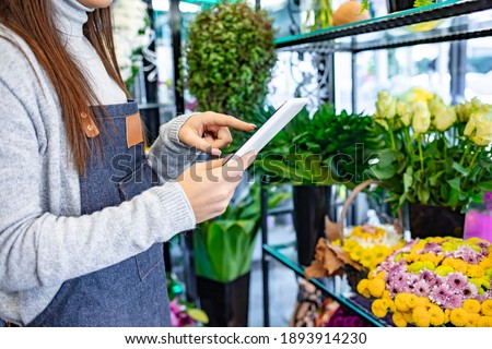 Young female florist using a digital tablet in her flower shop.  Small business. Beautiful female florist with tablet in flower shop. Florist using interface of online flower shop