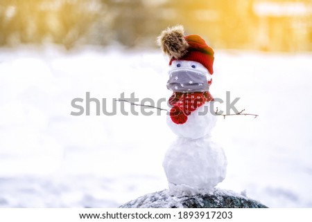Snowman in a hat in a disposable medical face mask on a blurred background of snow-covered trees in the snow