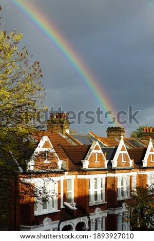 A double rainbow appearing to end behind a row of typical English terraced houses, against a stormy grey sky.  Image has copy space.