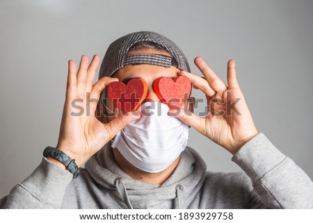 man with face mask holding heart over his eyes - Valentine's day