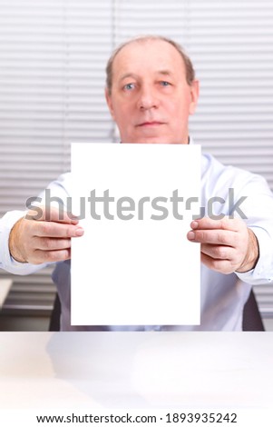 A man in an office at a computer holds a large sign in his hands. Vertical photo