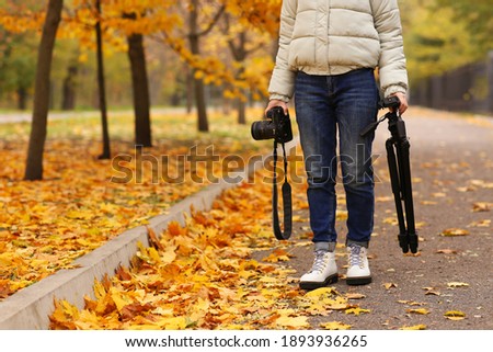 Photographer with professional camera and tripod outdoors on autumn day, closeup. Space for text