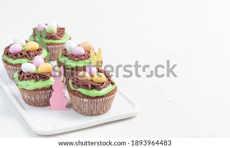 Carrot cupcakes with cream cheese frosting and Easter chocolate eggs, on a white plate, horizontal, copy space