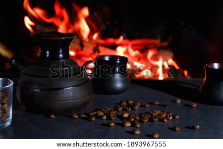 Cezve and coffee cups with coffee beans on the background of a burning fire. Turkish coffee.