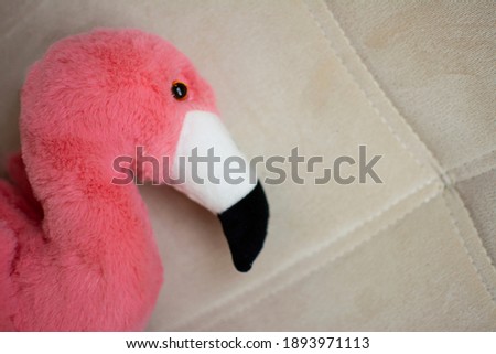 soft toy in the form of a fluffy pink flamingo with black eyes and a black and white beak on a light cream sofa. copy space. soft toys. holiday gifts. Valentines day. minimalistic. horizontal.