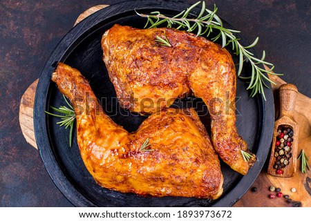 Baked chicken legs in a ceramic black baking dish on a wooden kitchen board. Grilled chicken, grilled chicken legs. Royalty-Free Stock Photo #1893973672