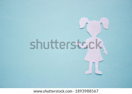 The form of a girl in a dress and with ponytails made of white paper, cut by hand. On the right side of the photo on a blue background with copy space