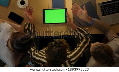 Top view creative people looking green screen tablet in office. Business woman demonstrating something to colleagues on mockup device in conference room. Young entrepreneurs working in coworking.