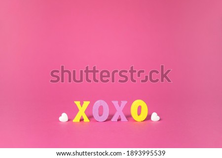 XOXO word in yellow and purple colors with white hearts on pink background. Love, hugs and kisses, Valentine Day greeting card with copy space.