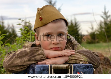 A boy in a military uniform holds an accordion in his hands. Victory Day. 9th May. A Great Victory.
