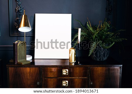 layout of the photo frame in a modern stylish interior, designer accessories table lamp and book holder. a golden candle and green house plants on a vintage wooden table.