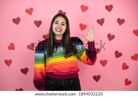 Young beautiful woman over pink background with harts doing hand symbol