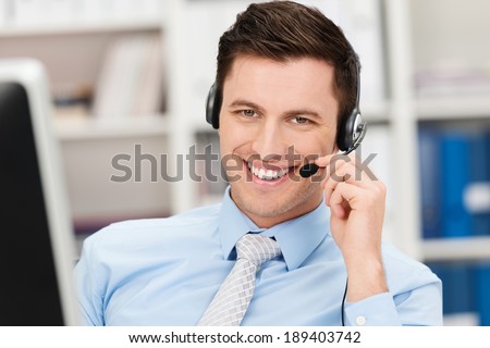 Handsome smiling young businessman using a headset conceptual of a call centre, client services, telemarketing or hands free office communication Royalty-Free Stock Photo #189403742